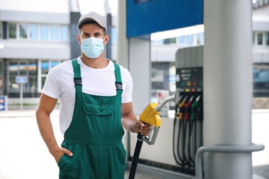 Photo of Worker in mask with fuel pump nozzle at modern gas station