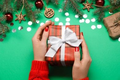 Woman holding gift box near fir tree branches with Christmas decor on green background, above view