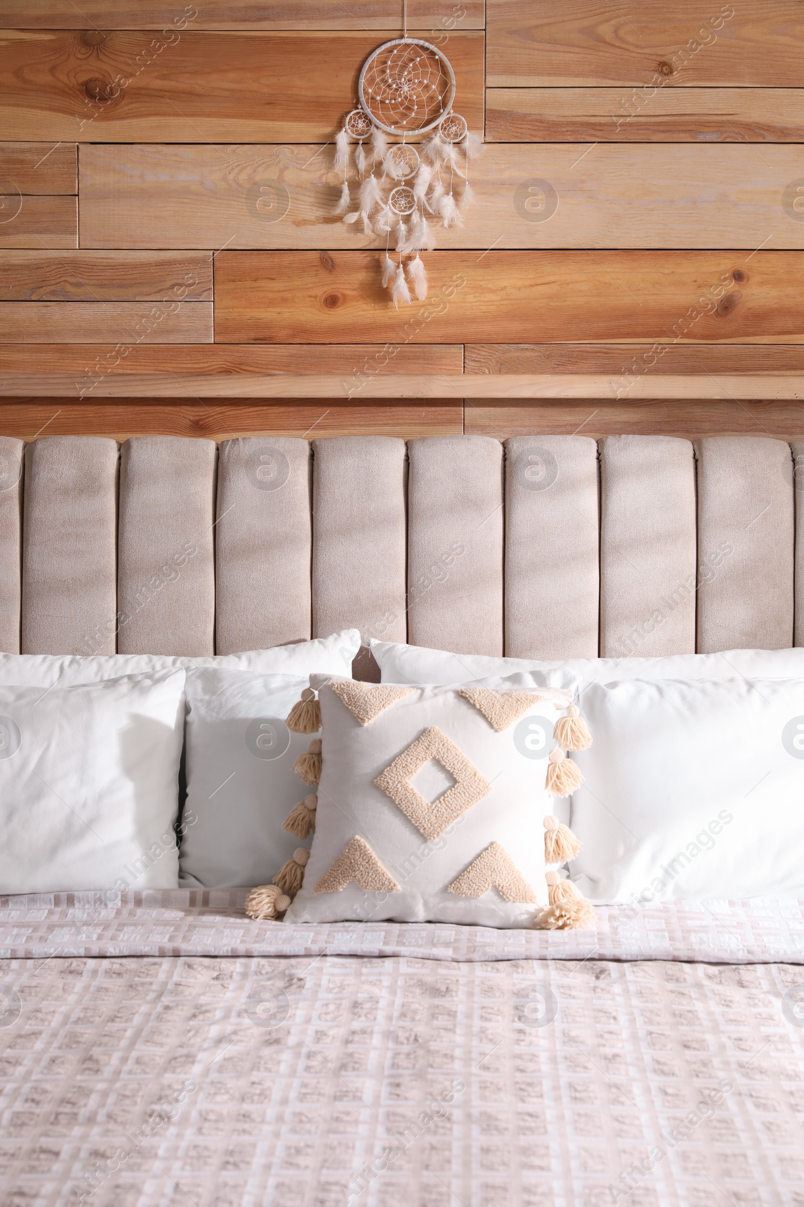 Photo of Beautiful dream catcher hanging above bed on wooden wall indoors