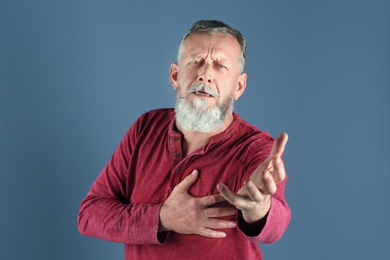 Mature man having heart attack on color background