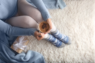 Woman wearing knitted socks on rug, top view. Warm clothes