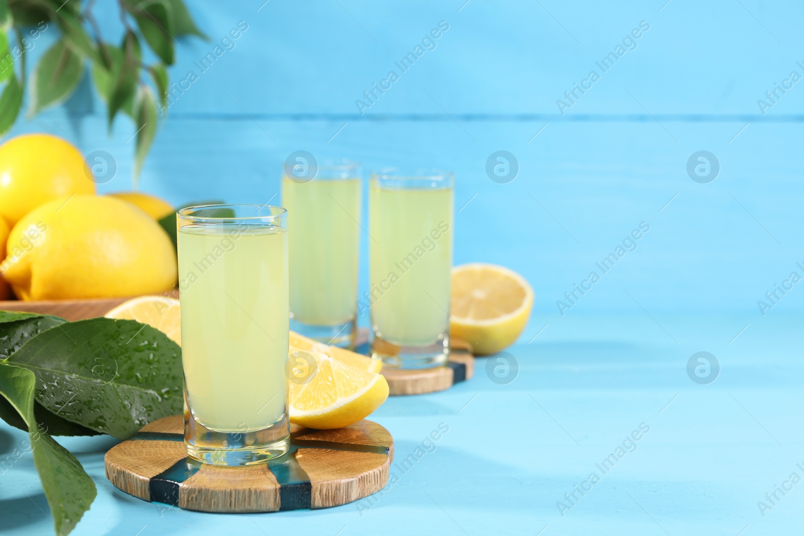 Photo of Tasty limoncello liqueur, lemons and green leaves on light blue table, space for text