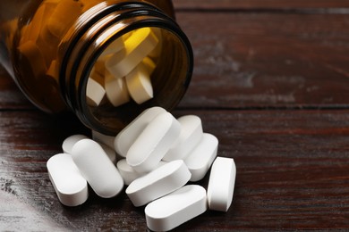 Photo of Bottle and vitamin pills on wooden table, closeup. Space for text