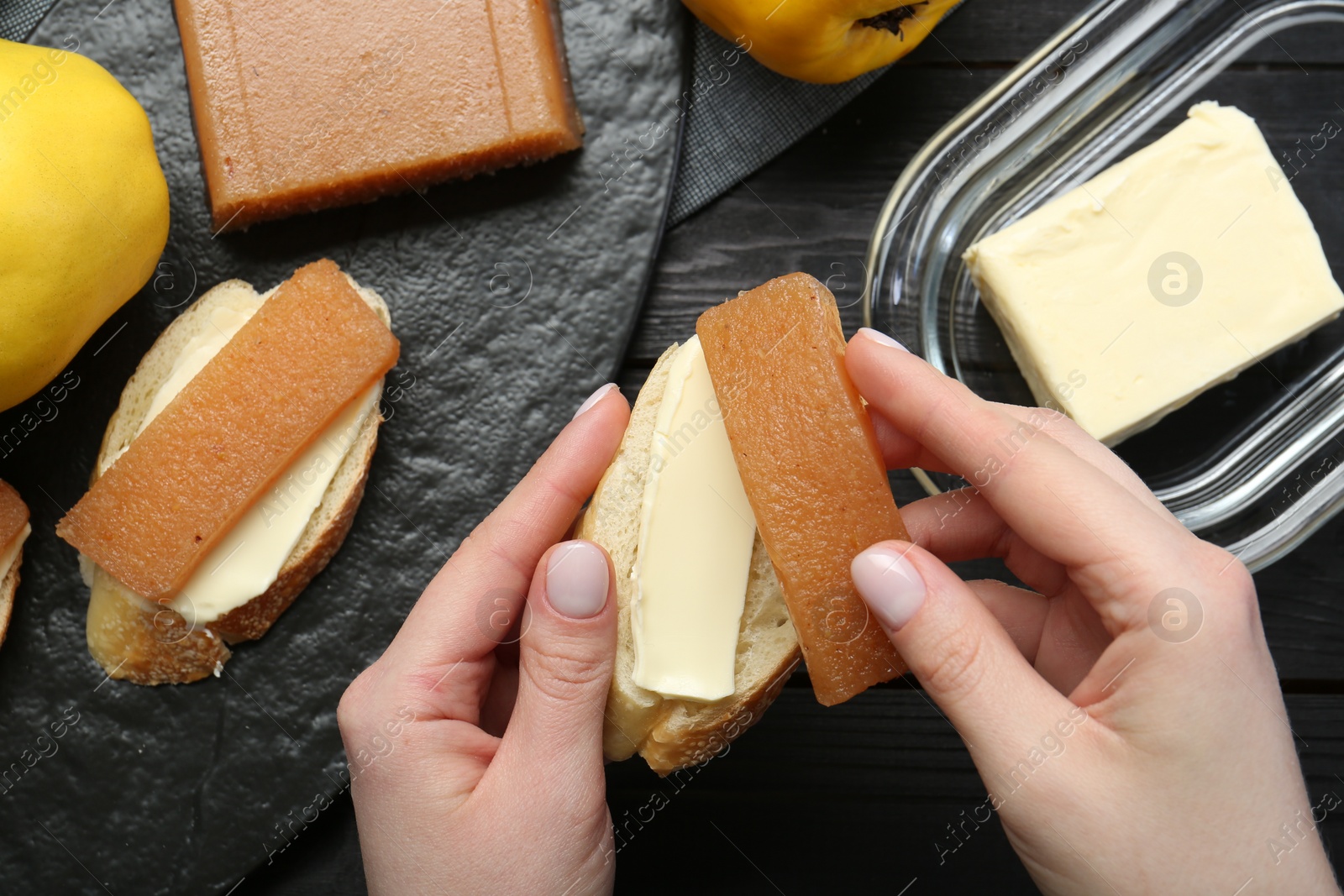 Photo of Woman making sandwich with quince paste at black wooden table, top view