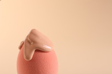 Photo of Pink makeup sponge with skin foundation on beige background, closeup. Space for text