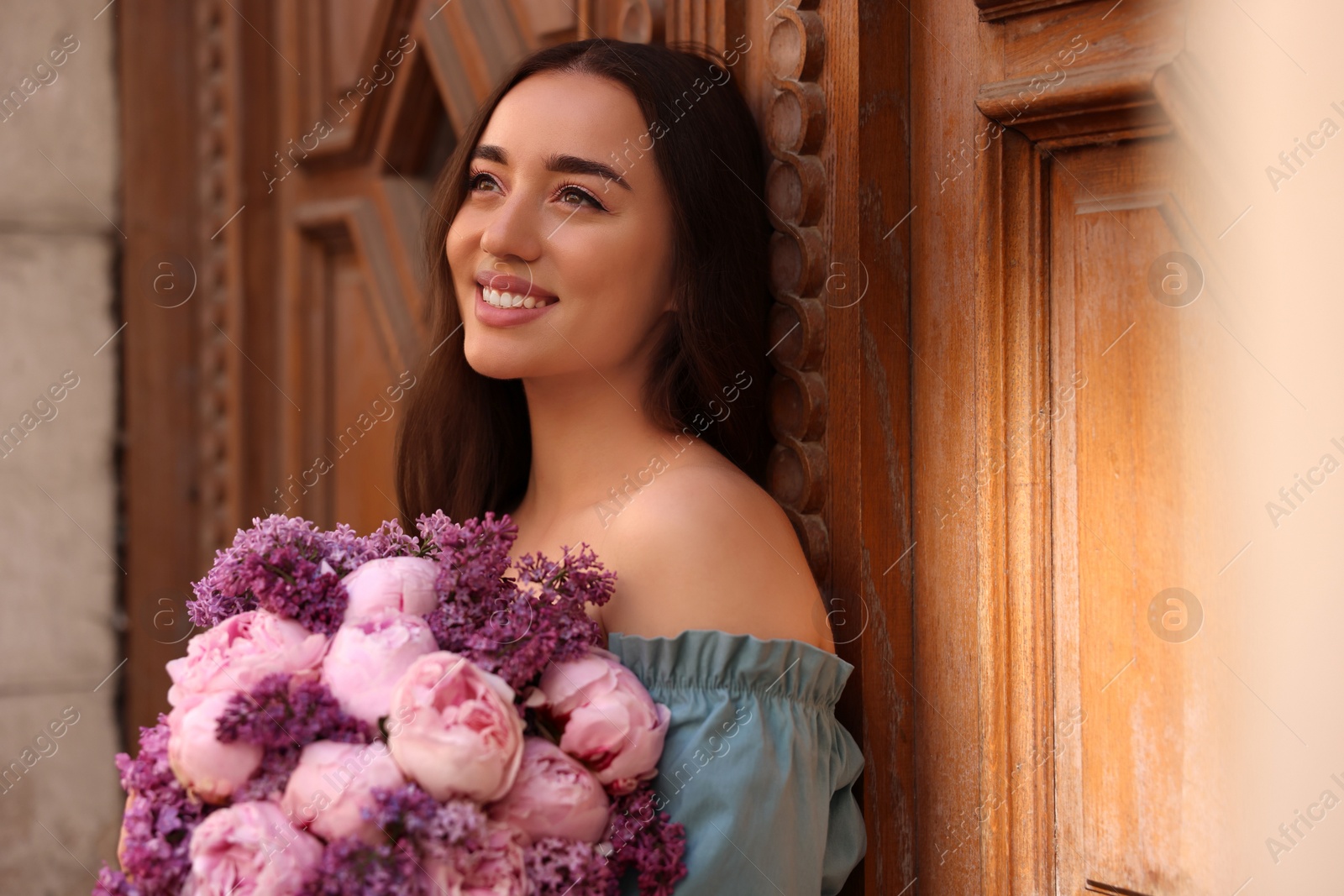 Photo of Beautiful woman with bouquet of spring flowers near building outdoors