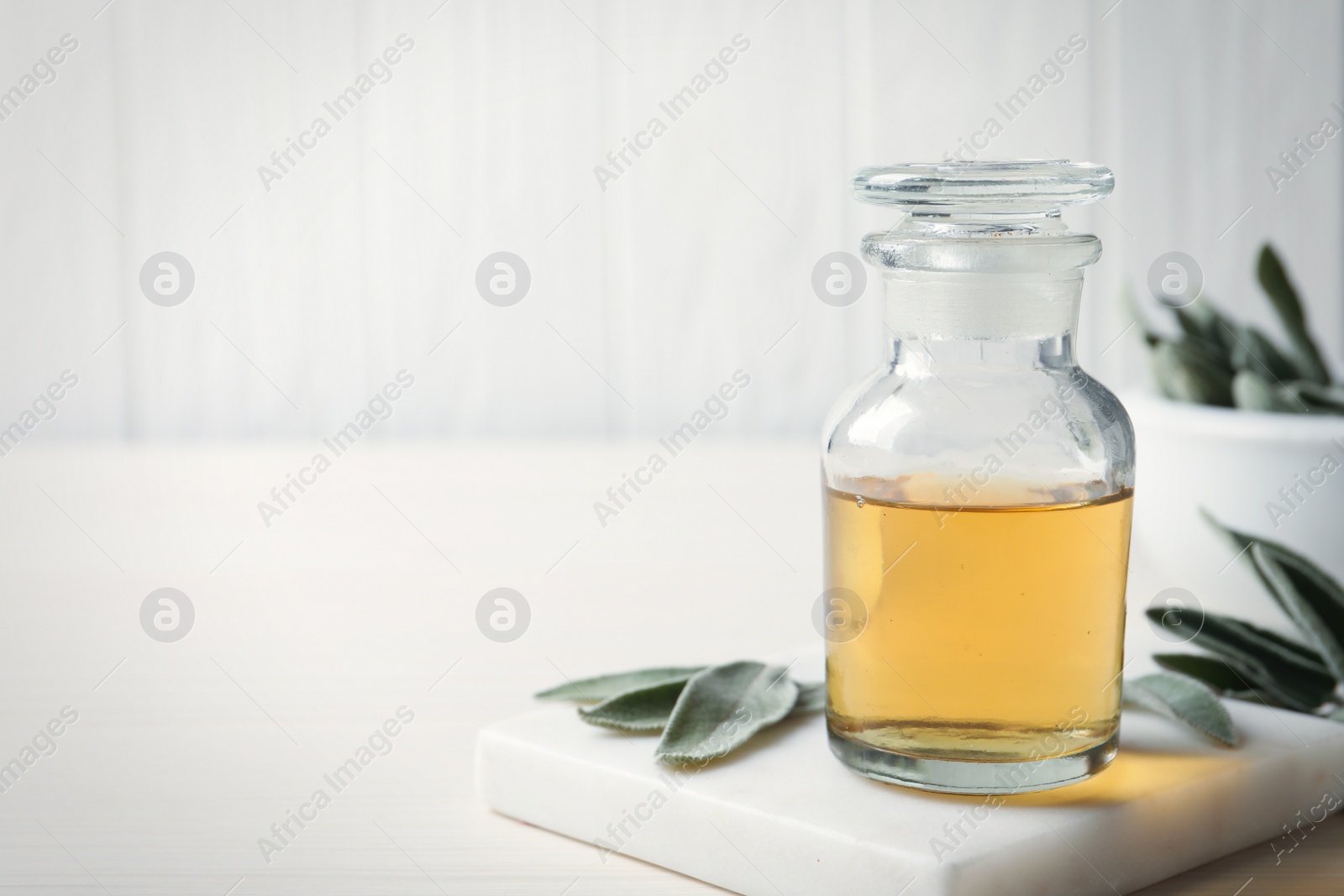 Photo of Bottle of essential sage oil and leaves on white wooden table. Space for text