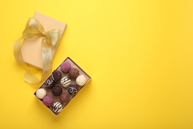 Photo of Open box with delicious chocolate candies on yellow background, top view. Space for text