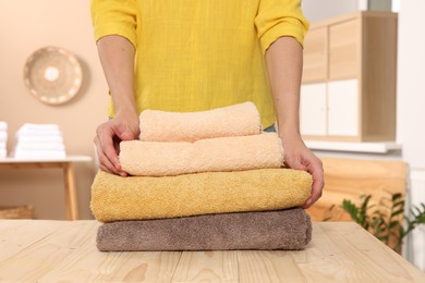Photo of Woman stacking clean towels on wooden table in laundry room, closeup