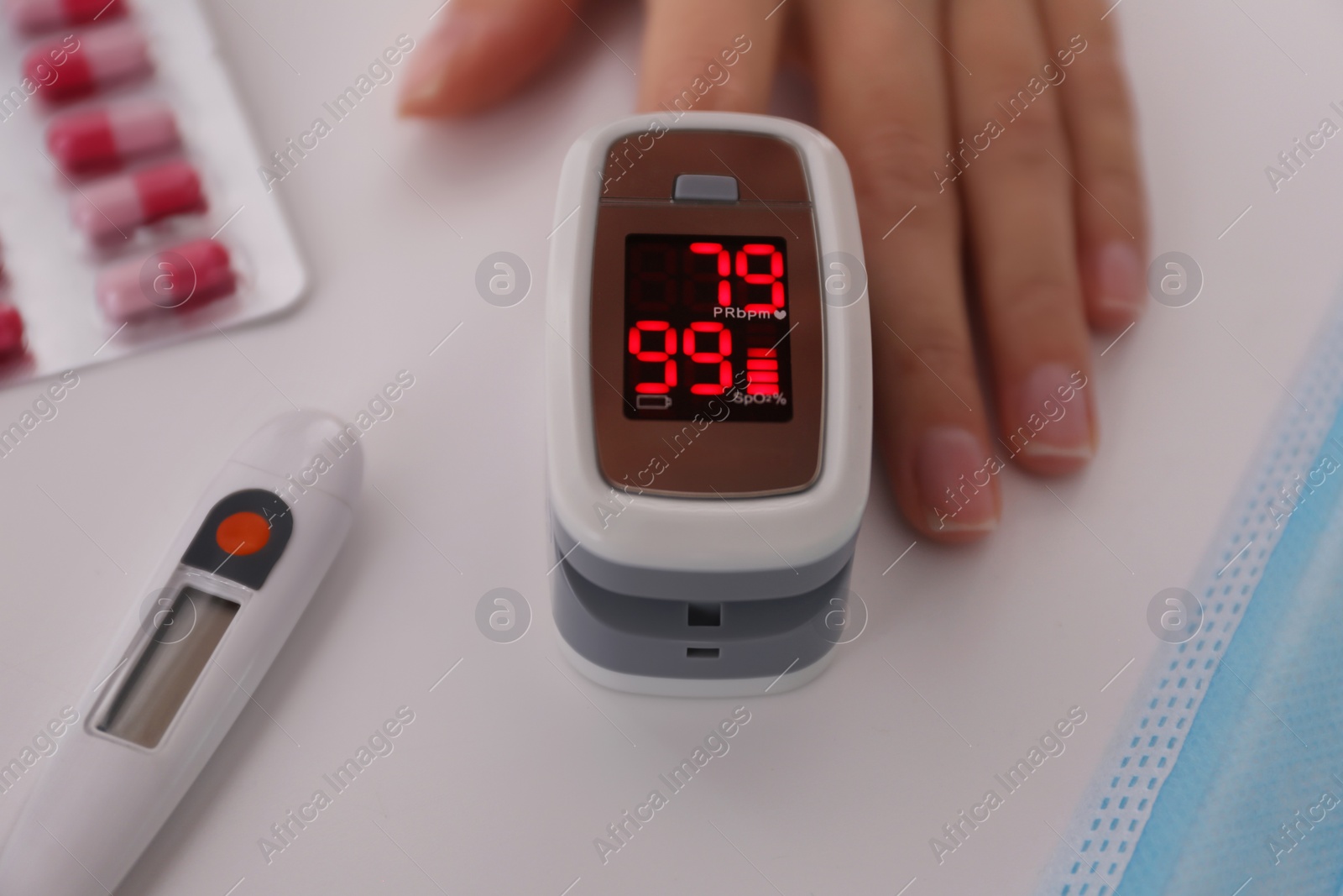 Photo of Woman measuring oxygen level with modern fingertip pulse oximeter at white table, closeup