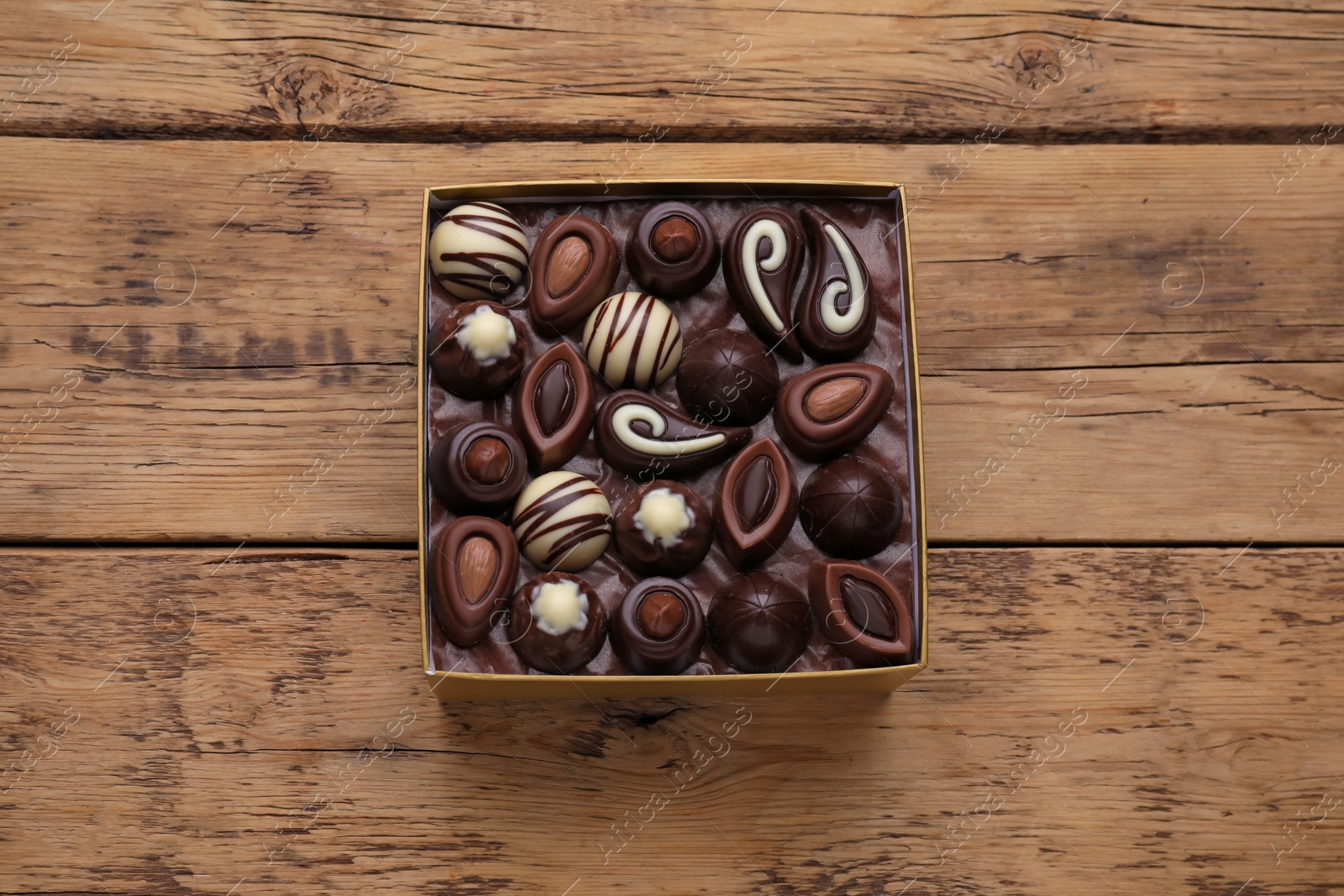 Photo of Box of delicious chocolate candies on wooden table, top view