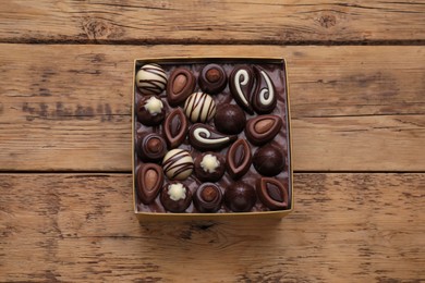 Photo of Box of delicious chocolate candies on wooden table, top view