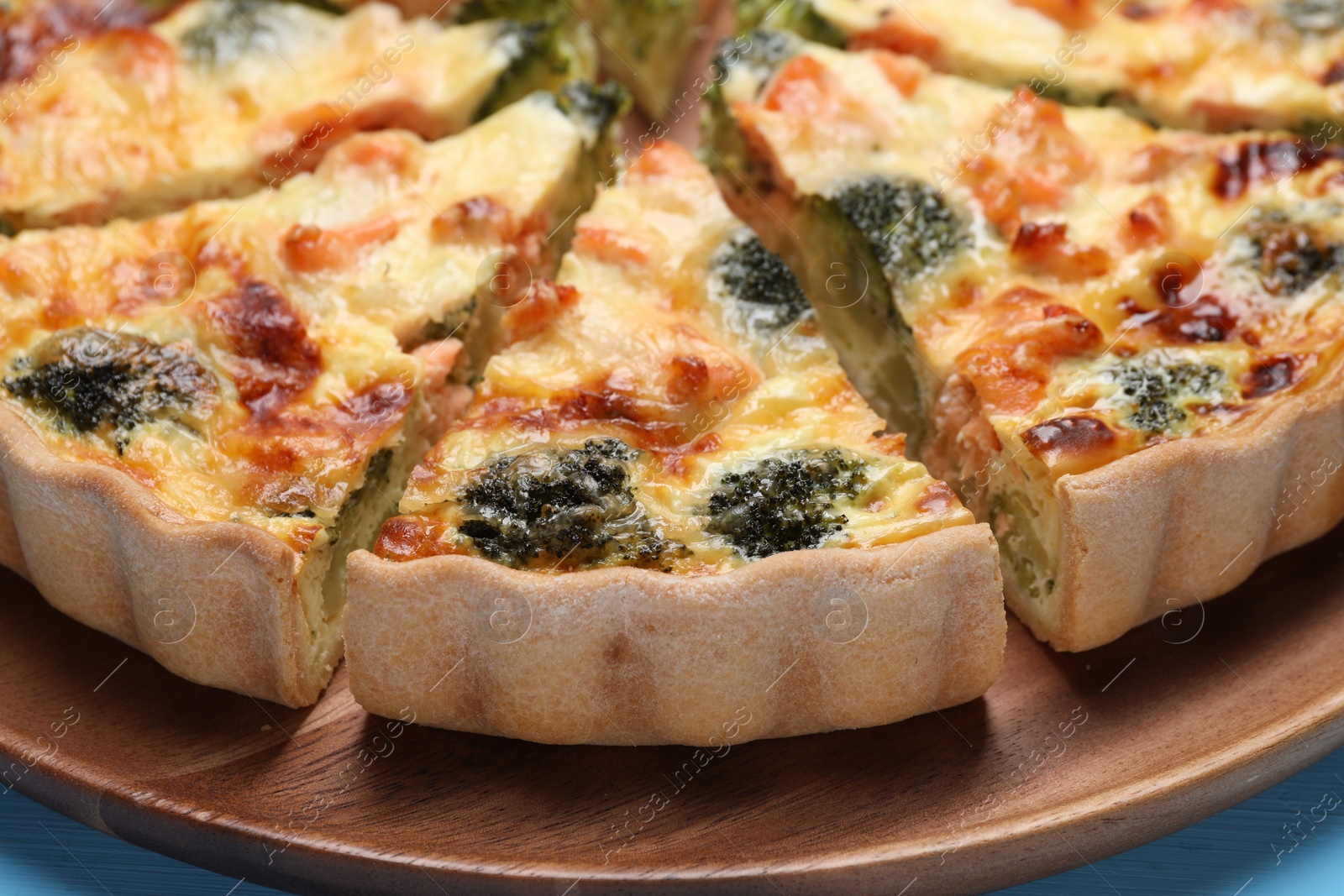 Photo of Delicious homemade quiche with salmon and broccoli on wooden board, closeup