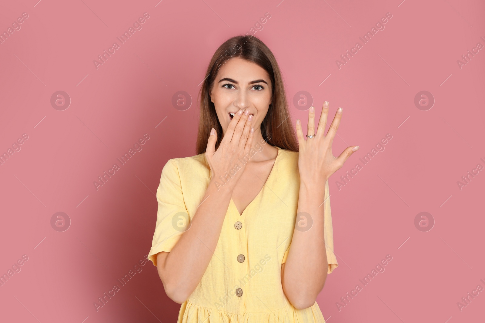 Photo of Happy young woman wearing beautiful engagement ring on pink background