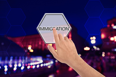 Image of Man touching button with word IMMIGRATION against night cityscape, closeup