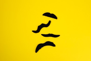 Photo of Different fake mustaches on yellow background, flat lay