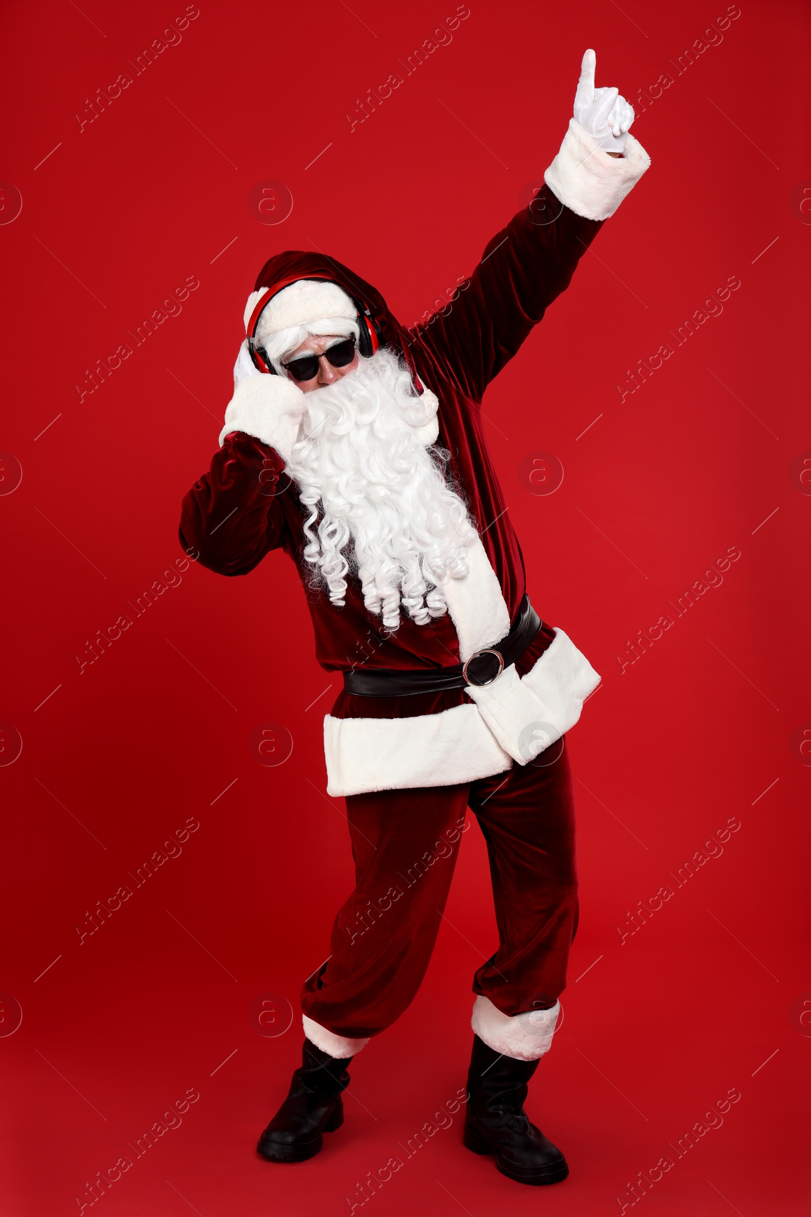 Photo of Santa Claus with headphones listening to Christmas music on red background