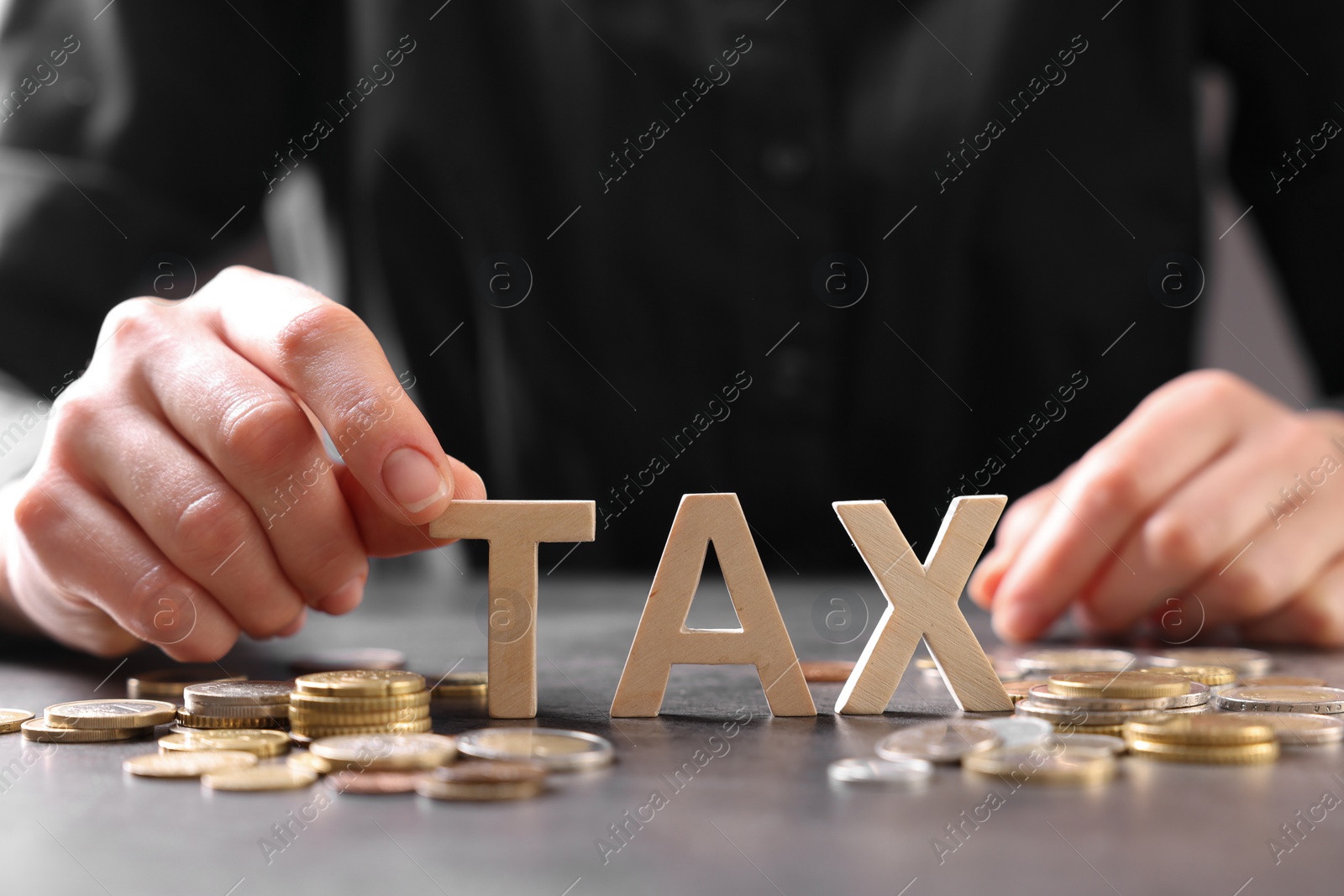 Photo of Woman with word Tax, wooden cubes and coins at grey table, closeup