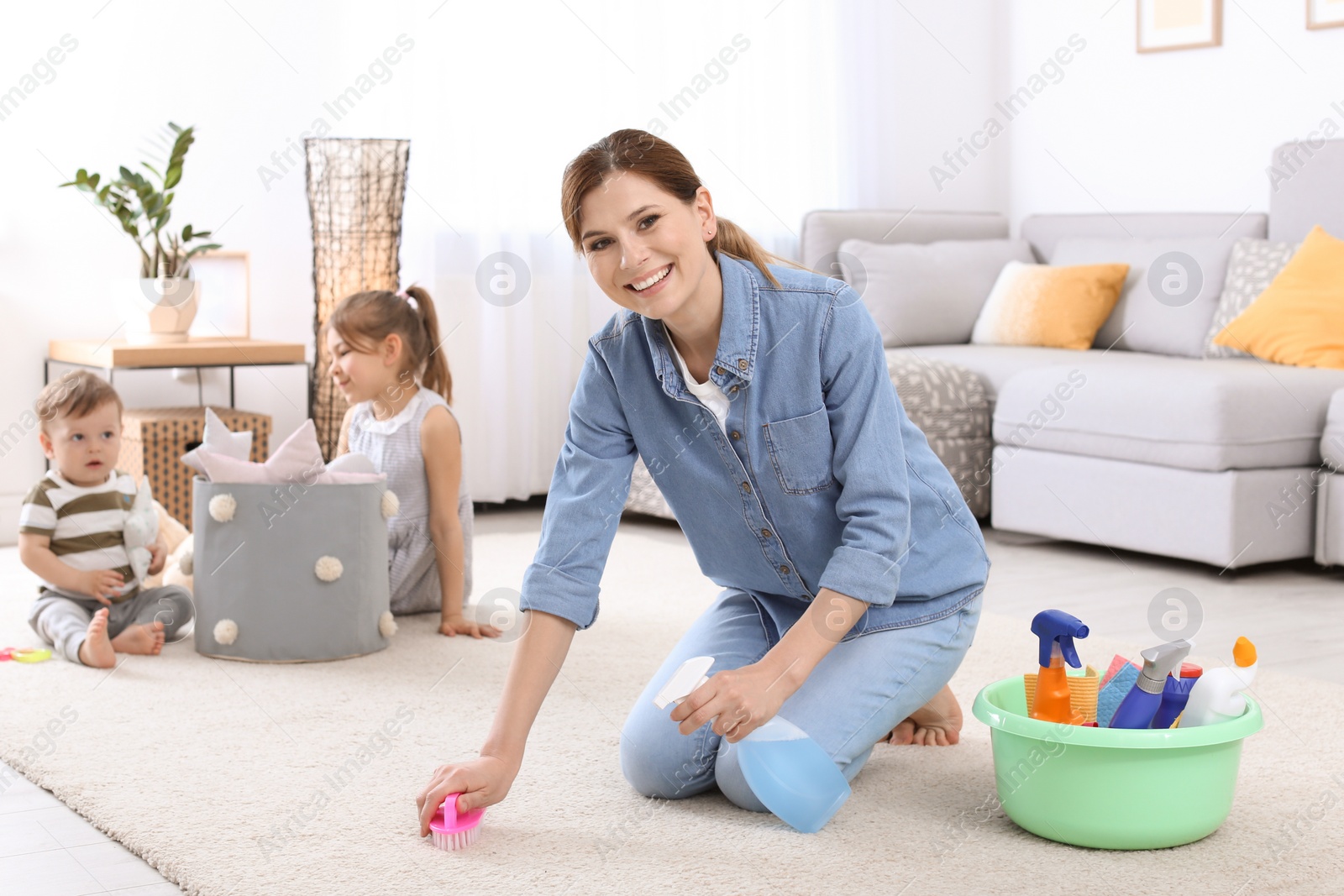 Photo of Housewife cleaning carpet while her children playing in room