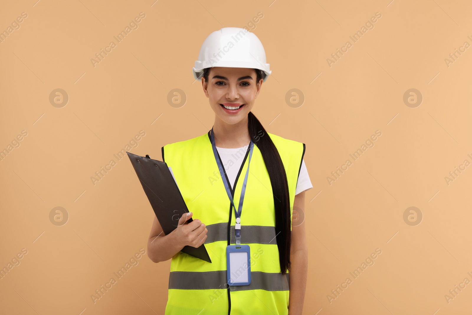 Photo of Engineer in hard hat holding clipboard on beige background