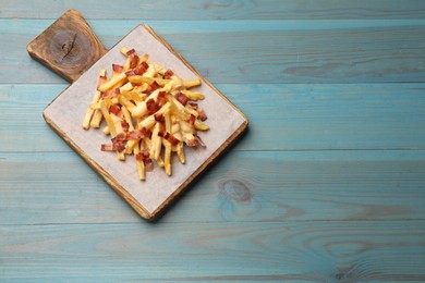 Photo of Delicious French fries with bacon and cheese sauce on light blue wooden table, top view. Space for text