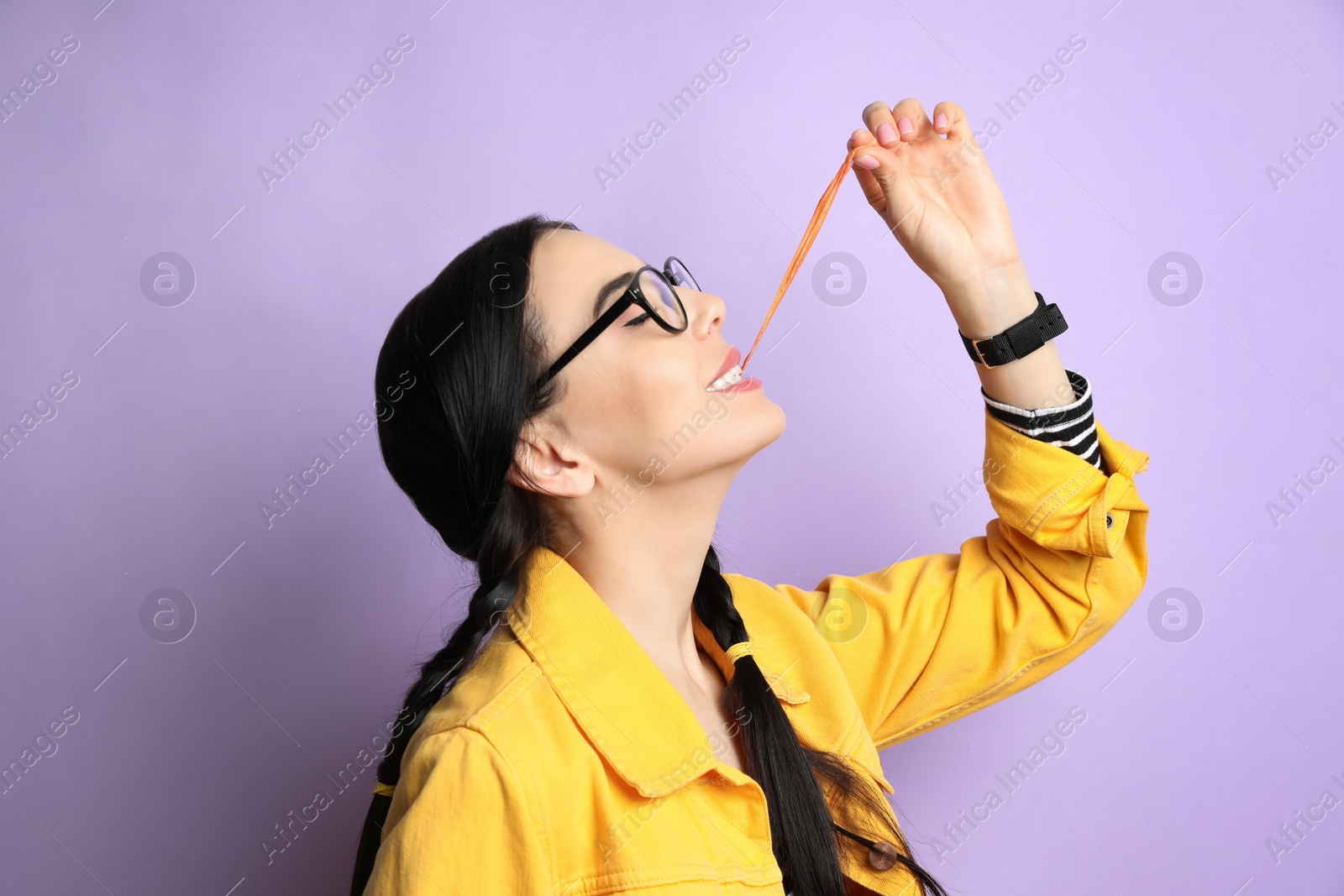 Photo of Fashionable young woman with braids chewing bubblegum on lilac background