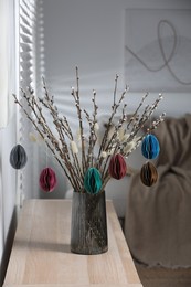 Beautiful pussy willow branches with paper eggs in vase on wooden table at home. Easter decor