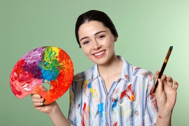 Photo of Woman with painting tools on pale green background. Young artist