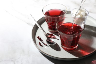 Photo of Making hibiscus tea. Pouring hot water into cup with roselle petals at white table. Space for text