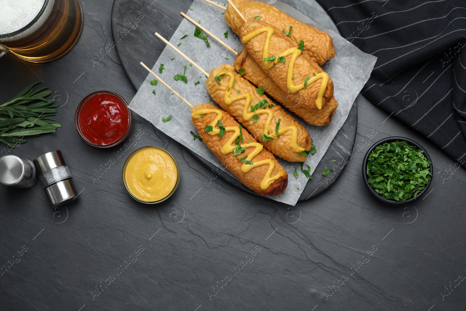 Photo of Delicious deep fried corn dogs and sauces on black table, flat lay
