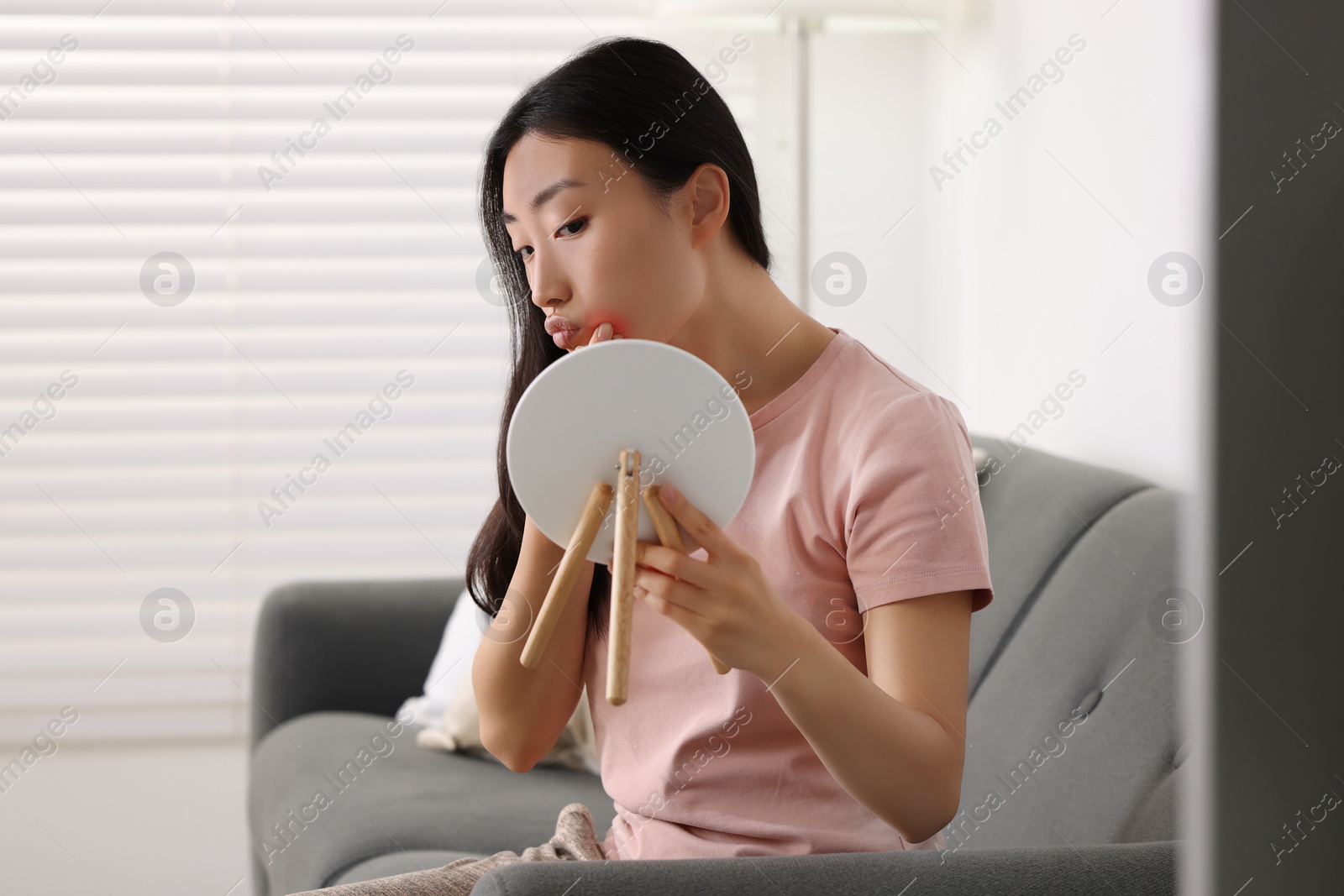 Photo of Suffering from allergy. Young woman with mirror checking her face in living room