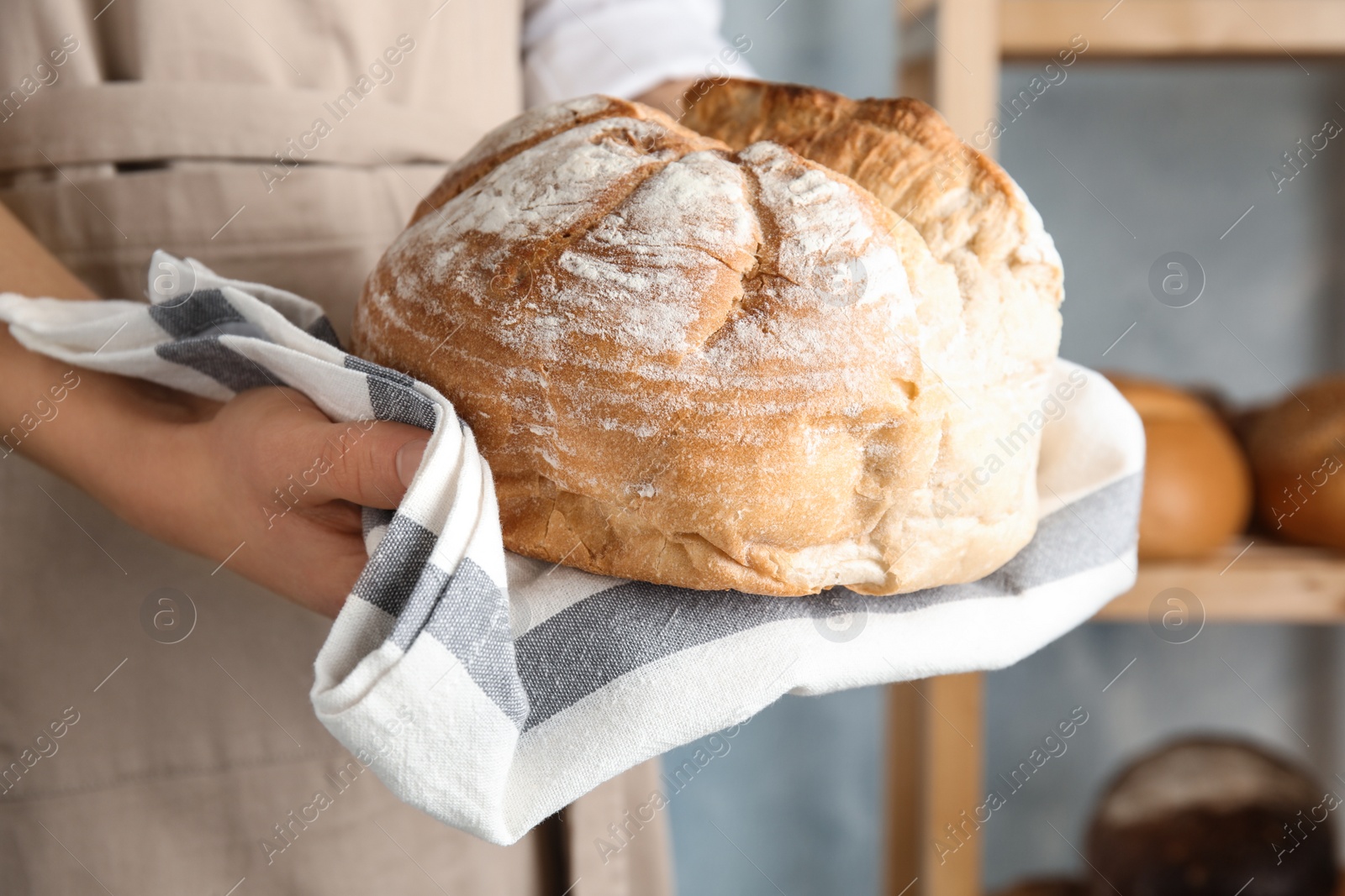 Photo of Baker holding loaf of bread indoors, closeup