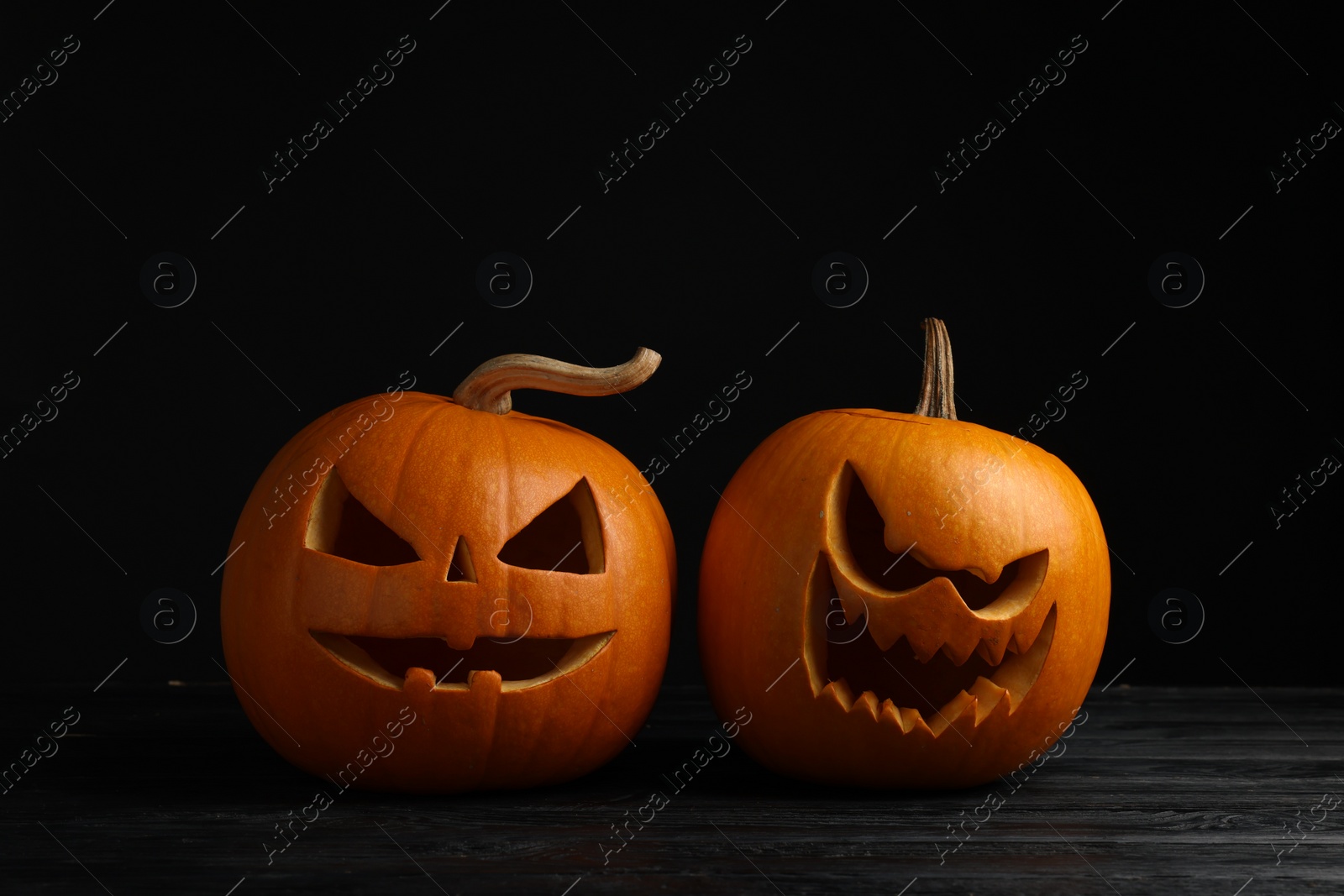 Photo of Scary jack o'lanterns made of pumpkins on wooden table against black background. Halloween traditional decor