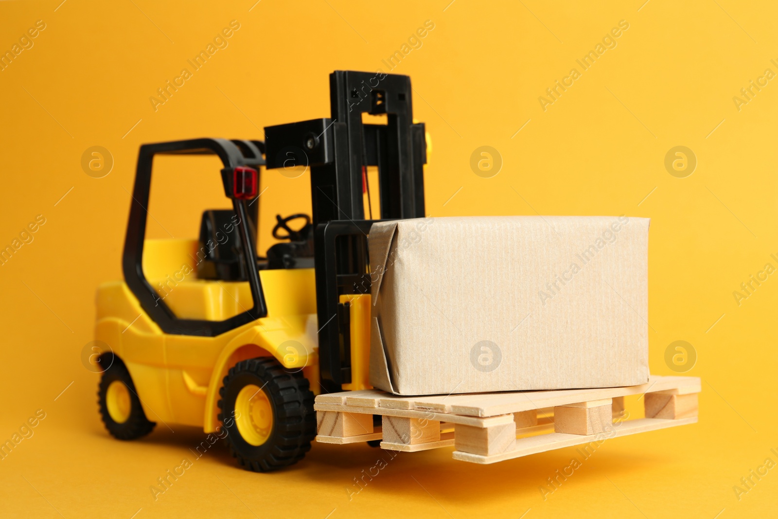 Photo of Toy forklift with wooden pallet and box on orange background
