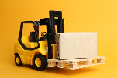 Toy forklift with wooden pallet and box on orange background