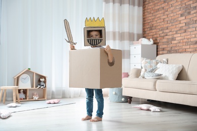 Photo of Cute little boy playing cardboard armor in living room