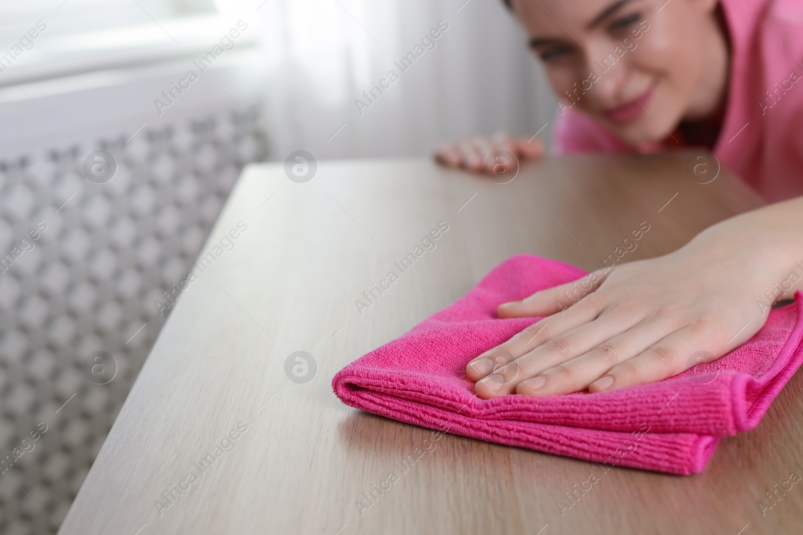 Photo of Young woman cleaning wooden table with rag at home, focus on hand. Space for text