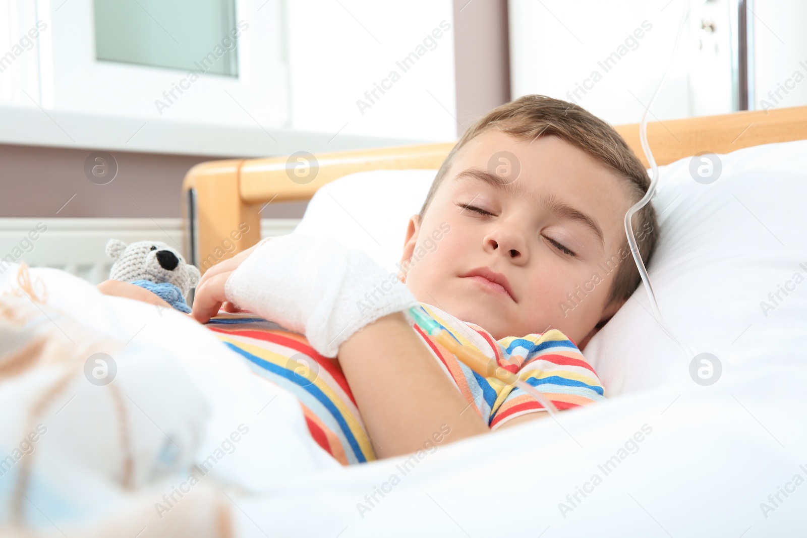 Photo of Little child with intravenous drip sleeping in hospital bed