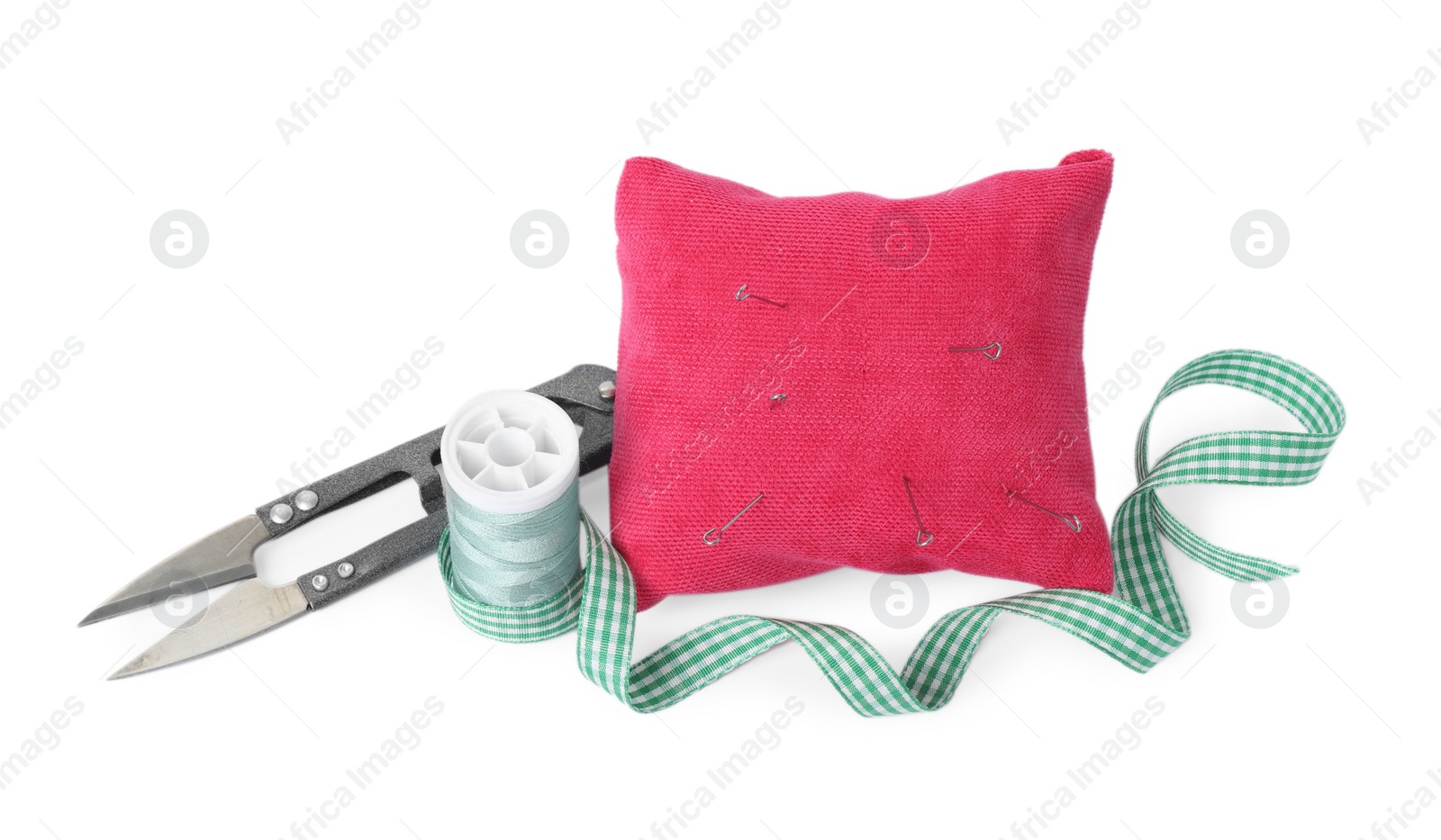 Photo of Pink pincushion, sewing needles, spool of thread, ribbon and cutter isolated on white