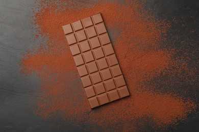 Photo of Tasty chocolate bar and cocoa powder on grey table, top view