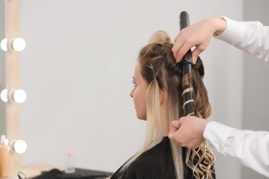 Hair styling. Hairdresser curling woman's hair in salon, closeup. Space for text