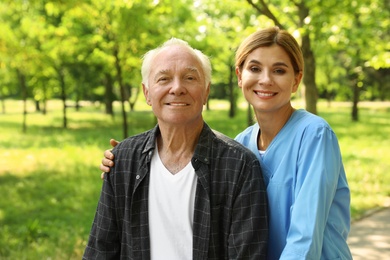 Photo of Portrait of happy elderly man and nurse in sunny park. Assisting seniors
