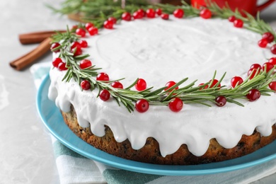 Traditional Christmas cake decorated with rosemary and cranberries on light grey marble table, closeup