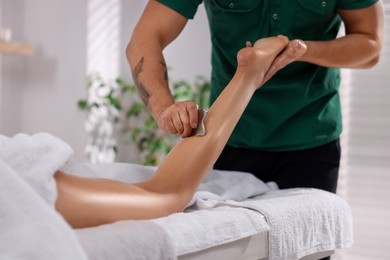 Woman receiving professional leg massage with gua sha on couch in spa salon, closeup