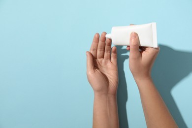 Woman applying cosmetic cream from tube onto her hand on light blue background, top view. Space for text