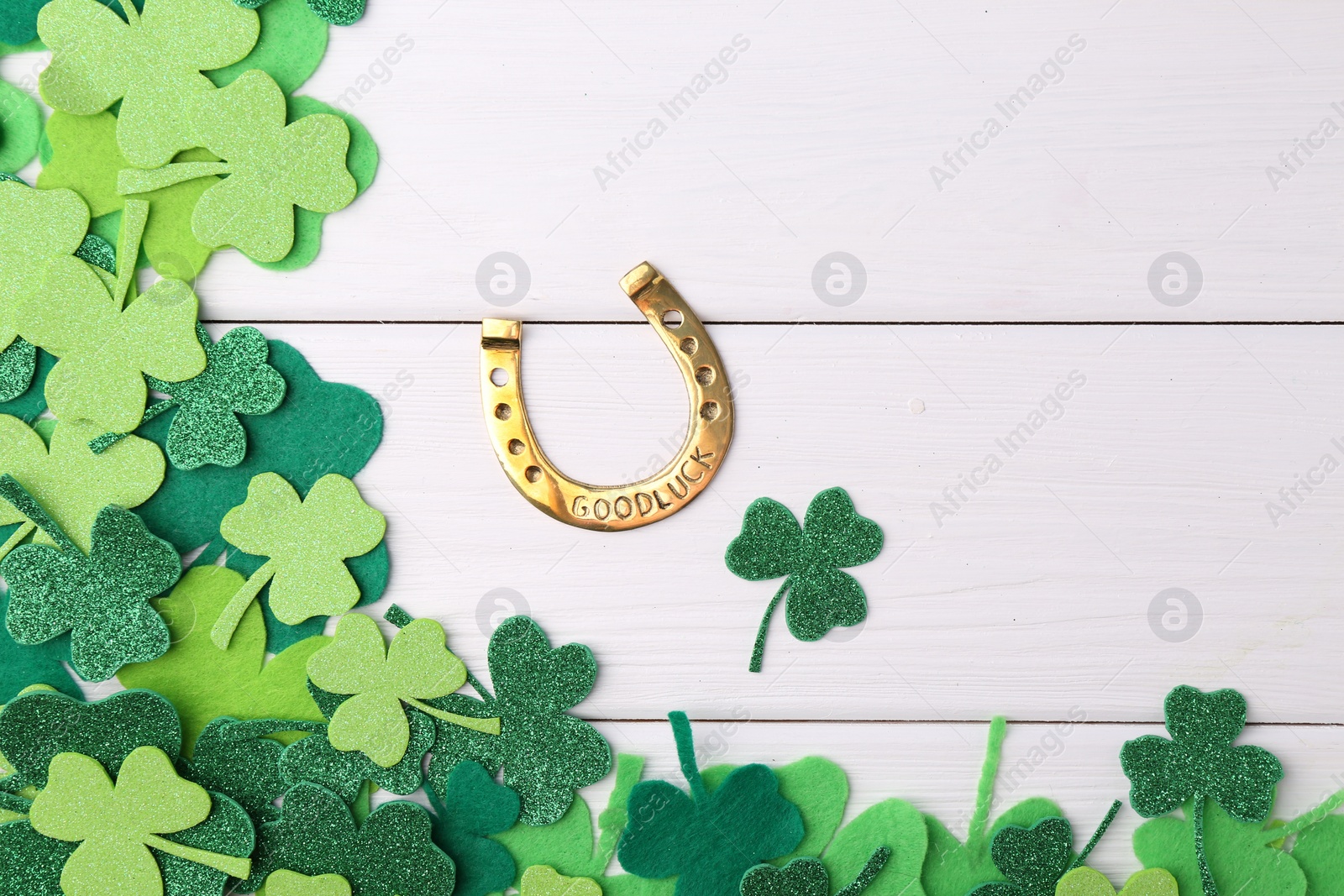 Photo of St. Patrick's day. Golden horseshoe and green decorative clover leaves on white wooden table, flat lay