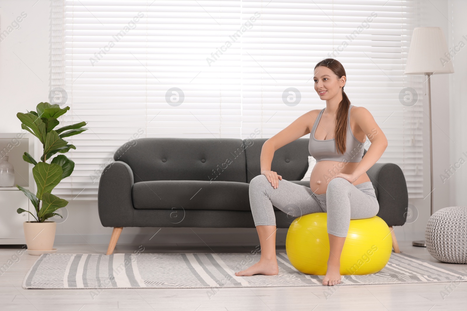 Photo of Pregnant woman sitting on fitness ball in room. Home yoga