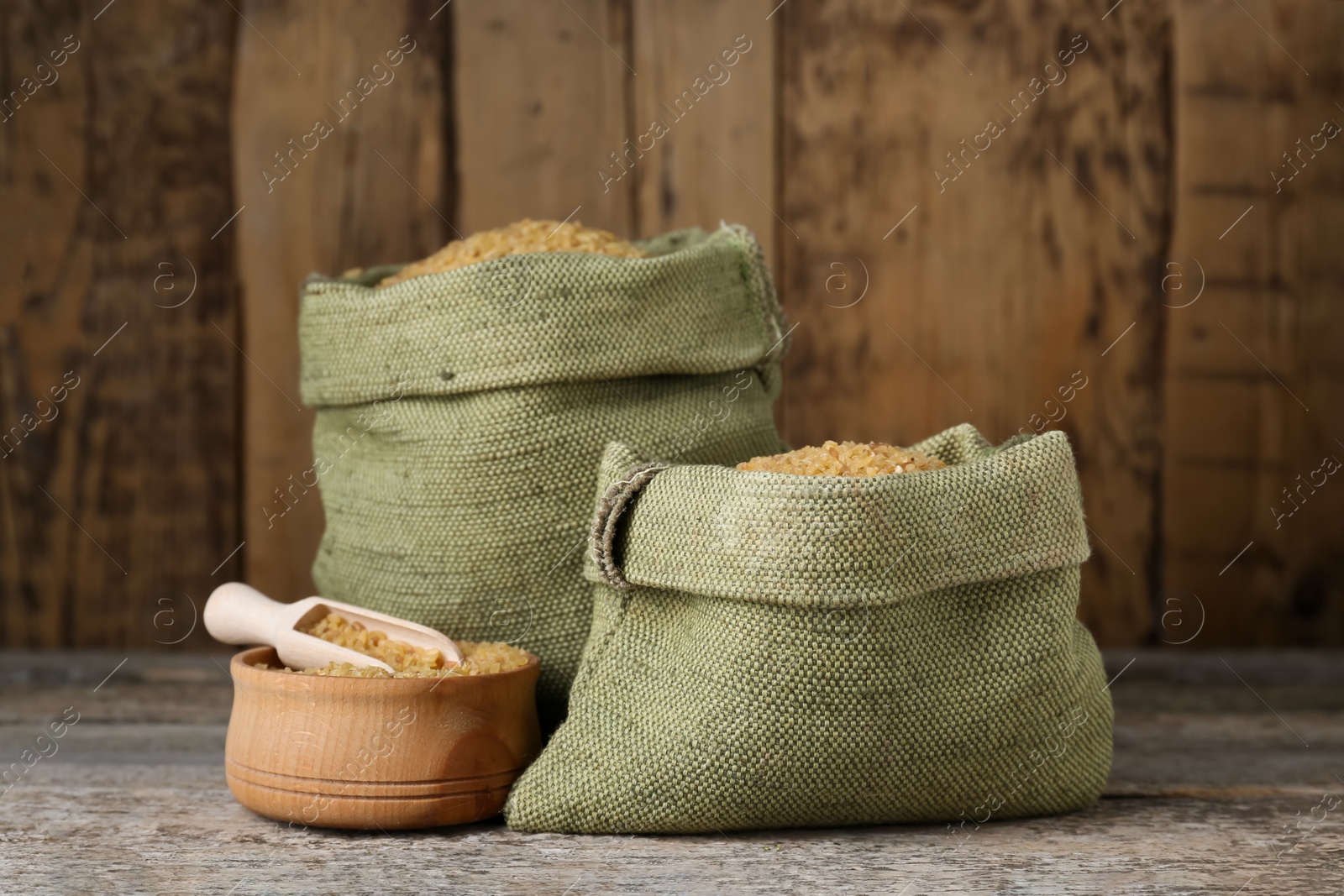 Photo of Burlap bags, scoop and bowl with uncooked bulgur on wooden table