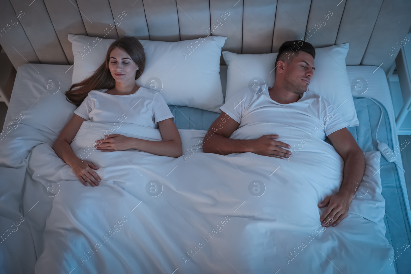 Photo of Couple sleeping on electric heating pad in bed at night, above view