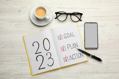 Photo of Flat lay composition of notebook with text 2023 Goal, Plan, Action on white wooden table. New year resolutions